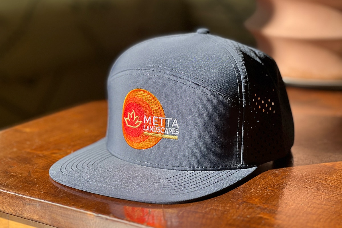A blue baseball cap featuring the Metta Landscapes logo in white showcases a stylish and professional brand identity.