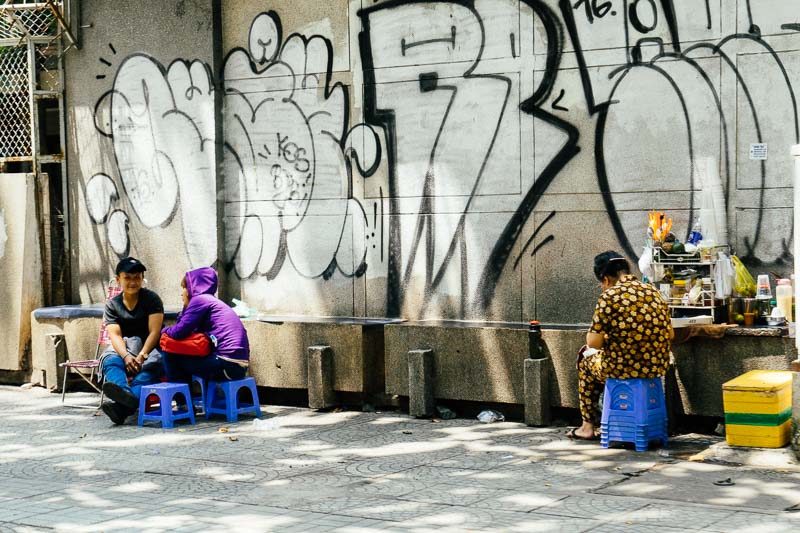 A graffiti wall with a woman selling street food Saigon Vietnam