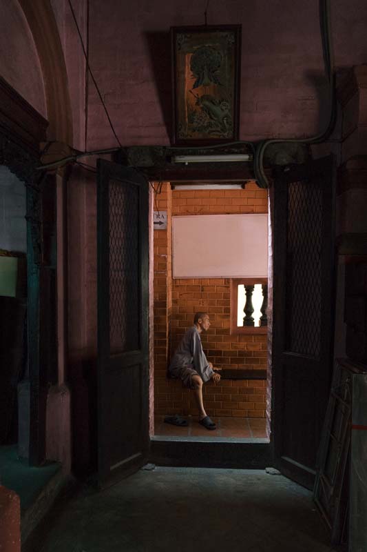 A monk sitting on a bench in an entryway of a temple in Saigon Vietnam