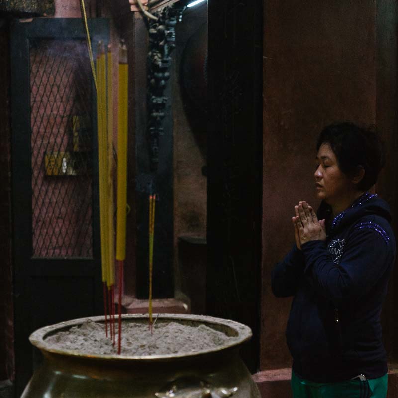 A woman, praying with incense, burning, and a temple in Saigon Vietnam