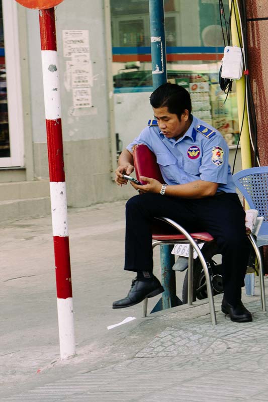 A man in a uniform on his break, looking at his cell phone and Saigon Vietnam