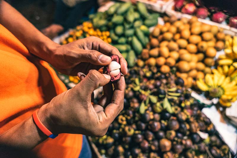 A tour guide, showing off a mangosteen at a stall at night market in Cambodia