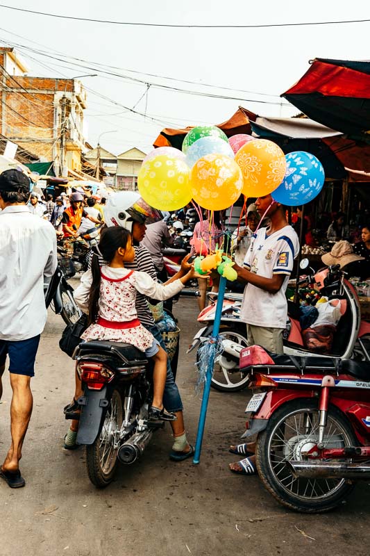 A market with a woman and her child, carrying some balloons in Cambodia
